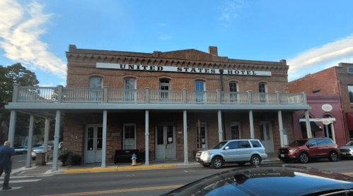 Historic United States Hotel building with a brick facade and balcony, located on a street with parked cars.