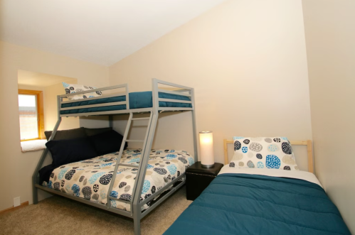 A cozy bedroom featuring a bunk bed and a single bed, both with patterned bedding and a bedside lamp.