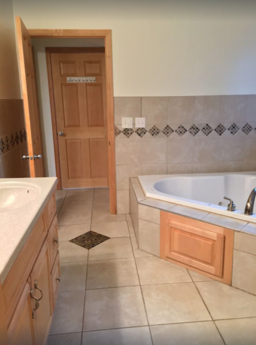 A spacious bathroom featuring a bathtub, wooden cabinetry, and a door leading to another room.