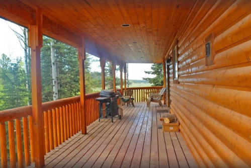 A wooden porch with a grill and seating, surrounded by trees and a scenic view.