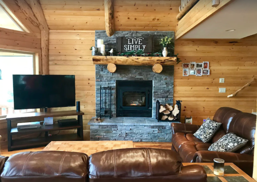 Cozy wooden living room with a stone fireplace, leather couches, and a "Live Simply" sign above the mantel.