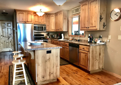 A rustic kitchen with wooden cabinets, stainless steel appliances, and a central island with three stools.