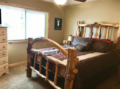 Cozy bedroom featuring a rustic log bed, patterned bedding, and a window with natural light.