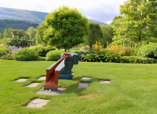 A colorful abstract sculpture in a lush garden, surrounded by greenery and mountains in the background.