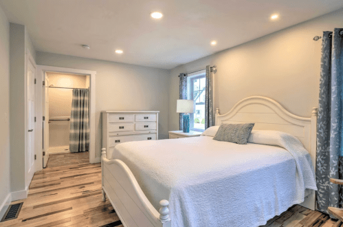 Bright bedroom featuring a white bed, dresser, and closet with light blue curtains and wooden flooring.