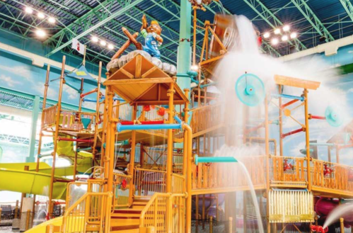 A colorful indoor water play structure with slides, water features, and a large statue of a character.