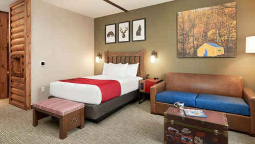 Cozy hotel room featuring a bed, sofa, and rustic decor with nature-themed artwork on the wall.