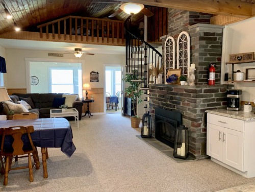 Cozy living room with a stone fireplace, dining area, and spiral staircase leading to a loft. Bright and inviting space.