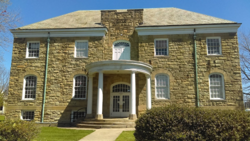 Historic stone building with a grand entrance, featuring columns and decorative stonework, set against a clear blue sky.