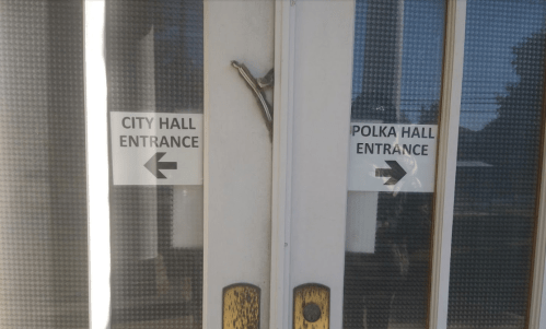 Two doors with signs: "City Hall Entrance" and "Polka Hall Entrance," each with an arrow pointing left.