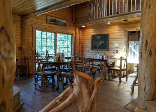 Cozy log cabin interior with wooden furniture, large windows, and natural light illuminating the space.