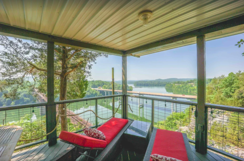 A scenic view from a balcony with red lounge chairs overlooking a river and lush green hills.