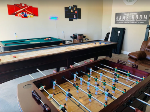 A game room featuring a foosball table, shuffleboard, pool table, and gaming decor on the walls.