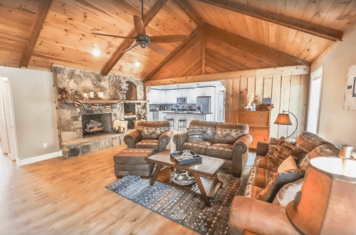 Cozy living room with wooden beams, stone fireplace, and comfortable seating, featuring warm tones and rustic decor.