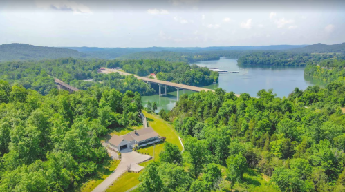 Aerial view of a lush green landscape with a river, bridge, and a building near the water's edge.
