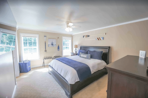 Bright bedroom with a large bed, light walls, and nautical decor, featuring windows and a ceiling fan.