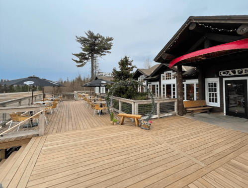 A wooden deck with outdoor seating at a café, surrounded by trees and a cloudy sky.