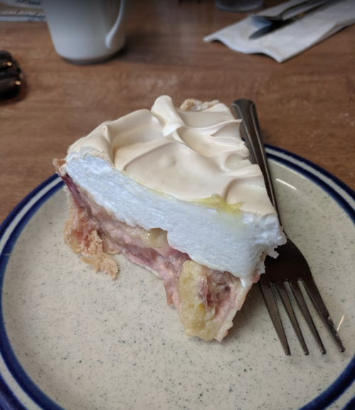 A slice of pie with a flaky crust, filled with fruit and topped with fluffy meringue, served on a plate with a fork.
