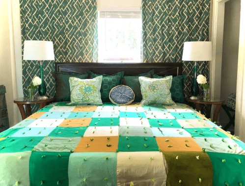 A cozy bedroom featuring a patchwork quilt in green and gold, with decorative pillows and patterned curtains.