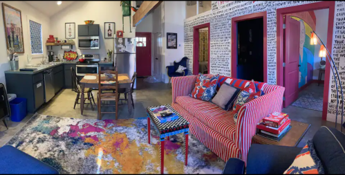 A colorful living space featuring a striped sofa, vibrant rug, dining area, and modern kitchen in a cozy setting.