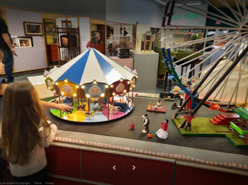 A child observes a detailed miniature carnival scene with a carousel and Ferris wheel.