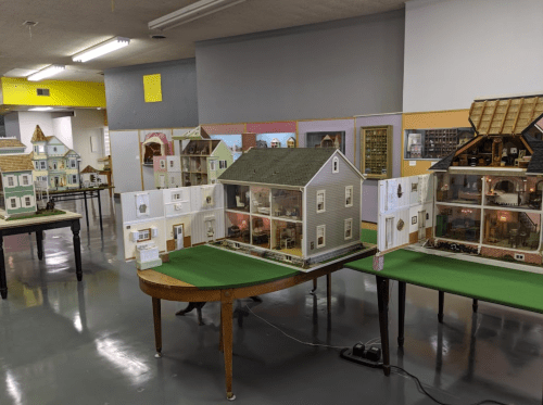 A display of several detailed dollhouses on tables in a spacious room with bright walls.