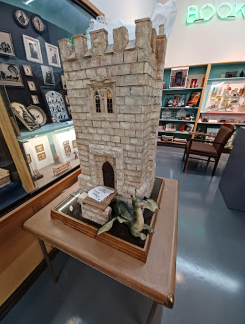 A decorative castle model with a dragon at its base, displayed in a museum-like setting.