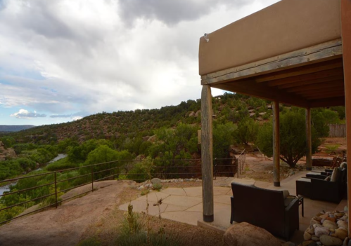 A scenic view from a patio overlooking a river and lush greenery, with mountains in the background under a cloudy sky.