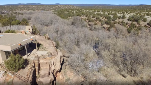 Aerial view of a rocky cliff with a building, surrounded by bare trees and a vast landscape of hills and valleys.