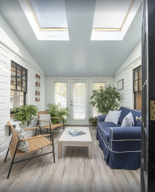 Bright sunroom with skylights, a blue couch, plants, and a wooden coffee table, featuring light wood flooring.