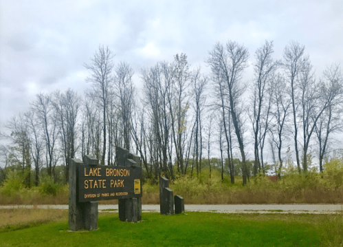 Sign for Lake Bronson State Park with trees in the background under a cloudy sky.