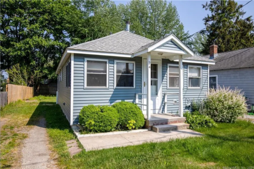 A small blue house with a front porch, surrounded by greenery and a clear sky.