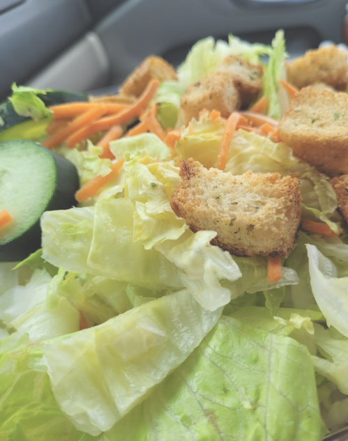 A close-up of a fresh salad with lettuce, cucumber slices, shredded carrots, and croutons.