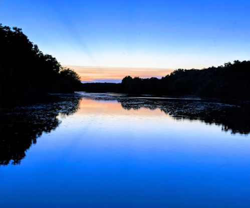 A serene river at sunset, reflecting vibrant blue and orange hues, surrounded by trees.