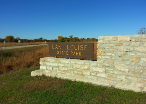 Sign for Lake Louise State Park, set against a clear blue sky and grassy landscape.