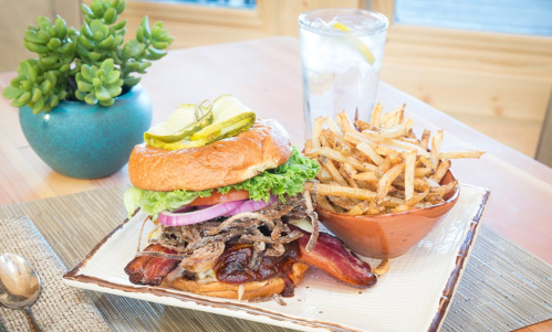 A delicious burger topped with lettuce, tomato, onion, and pickles, served with crispy fries and a drink.