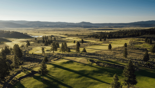 A scenic view of a golf course surrounded by rolling hills and trees under a clear blue sky.
