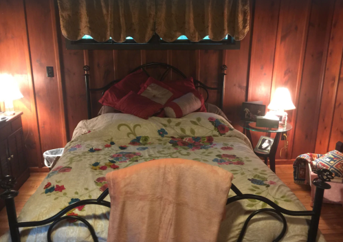 Cozy bedroom with a floral bedspread, wooden walls, and soft lighting from bedside lamps.