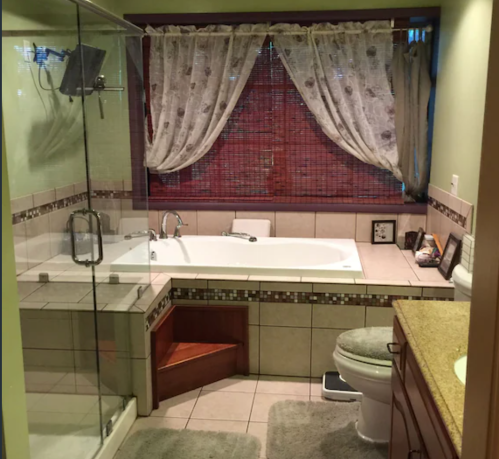 A cozy bathroom featuring a glass shower, a large bathtub, and natural light from a window with sheer curtains.