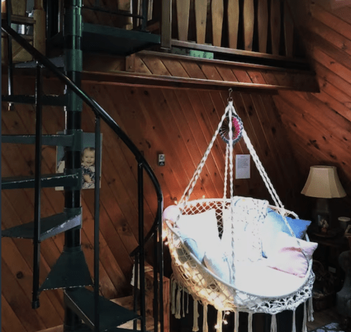 A cozy interior featuring a spiral staircase and a hanging macrame chair with cushions, illuminated by soft lights.