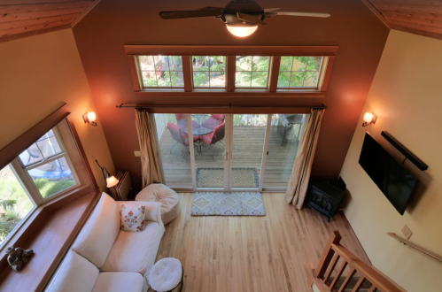A cozy living room with a white sofa, large windows, and a view of a deck with outdoor seating.