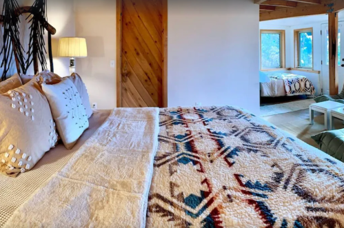 Cozy bedroom with a patterned blanket, decorative pillows, and large windows overlooking a serene view.
