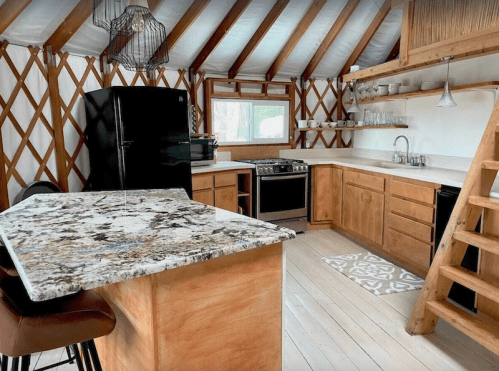 Cozy kitchen in a yurt with wooden beams, granite countertops, and modern appliances. Bright and inviting space.