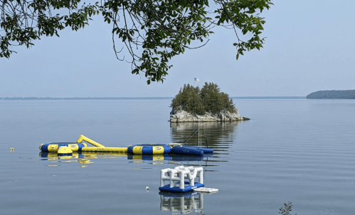 A calm lake scene featuring a small island and colorful inflatable structures floating on the water.