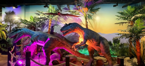 Two dinosaur sculptures in a vibrant, tropical setting with palm trees and a colorful backdrop.