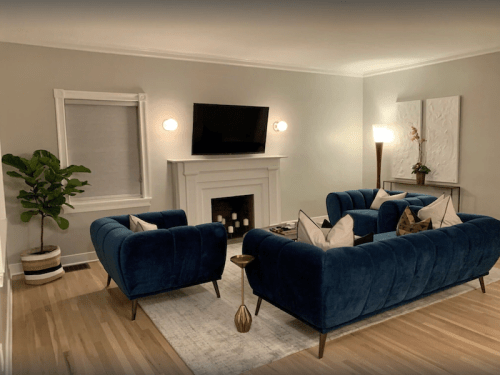 A cozy living room with blue sofas, a TV, a fireplace, and a plant, featuring warm lighting and modern decor.