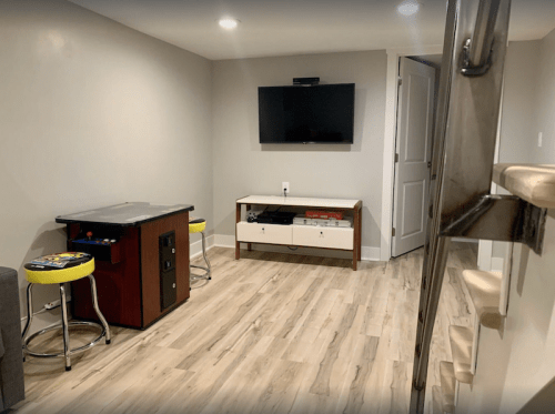 Cozy basement room with a TV, a small table, two stools, and light-colored flooring.