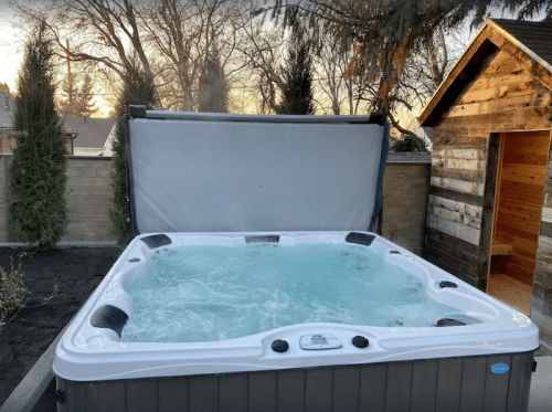 A hot tub with bubbling water, surrounded by trees and a wooden shed, under a clear sky.