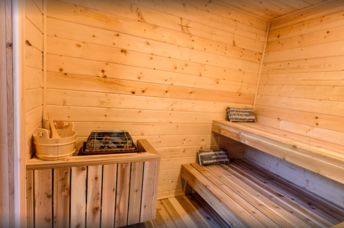 A wooden sauna interior featuring benches, a heater, and a bucket, all in a warm, natural wood finish.