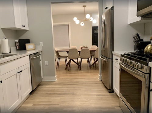 Modern kitchen with stainless steel appliances, leading to a dining area with a round table and stylish chairs.